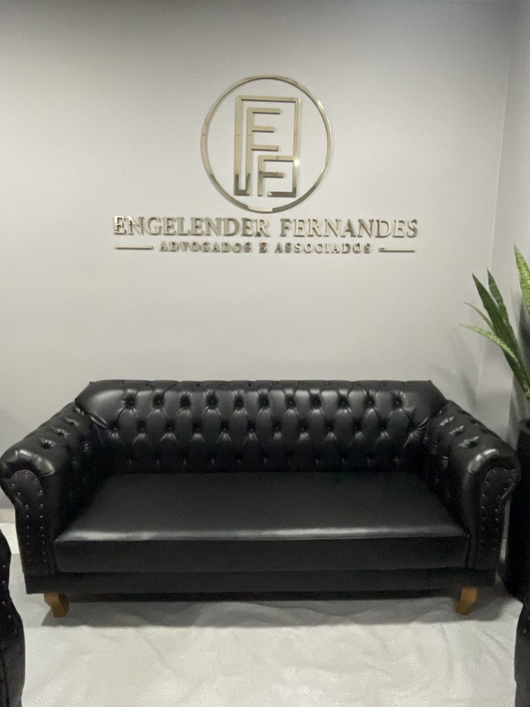 Parede da recepção com o logotipo Engelender Fernandes em dourado sobre o sofá chesterfield